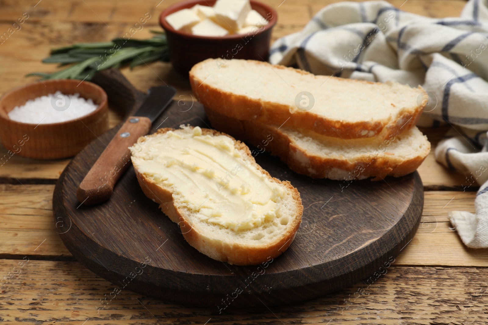 Photo of Fresh bread with butter and knife on wooden table, closeup