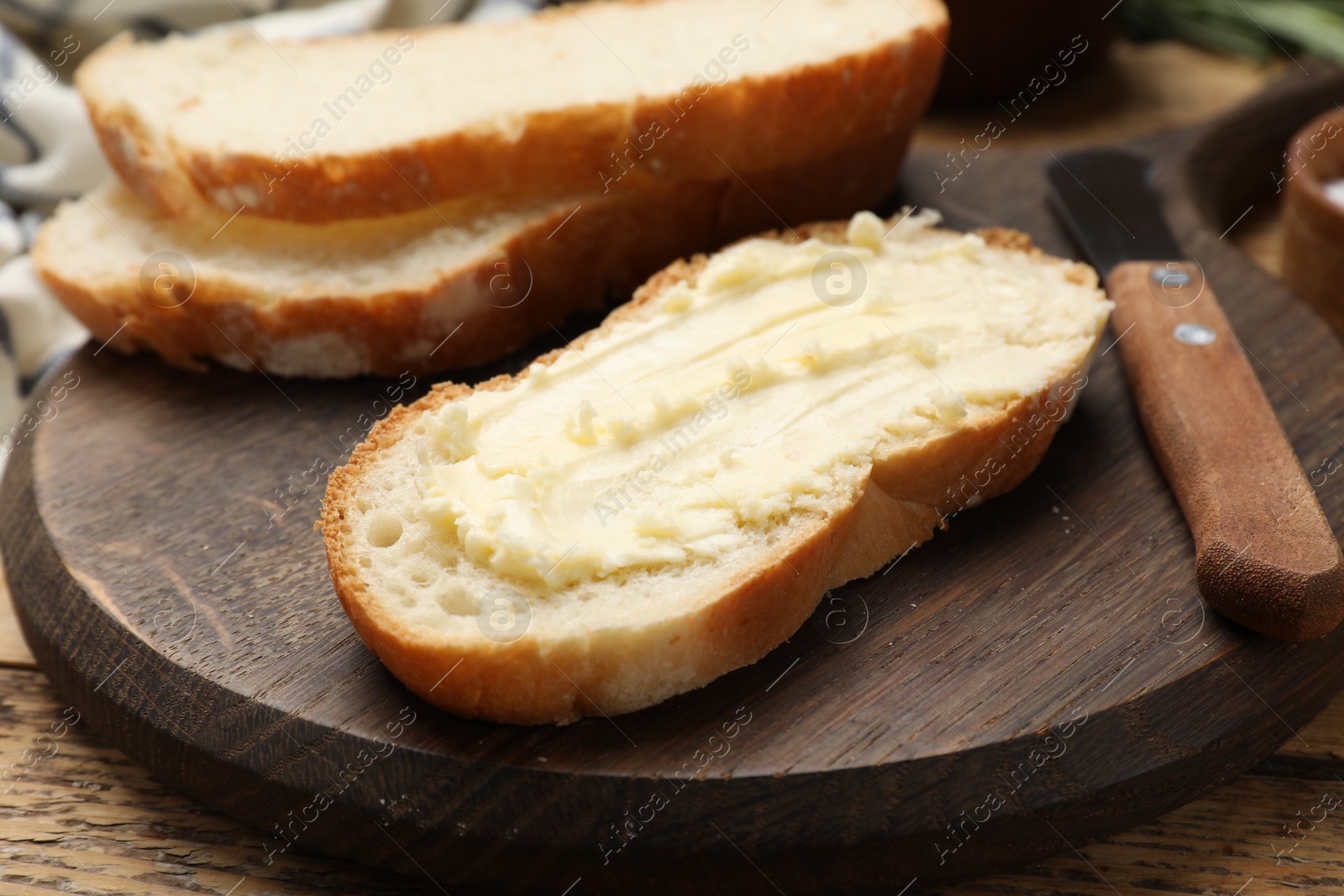 Photo of Fresh bread with butter and knife on wooden table, closeup