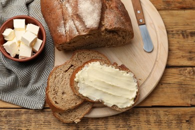 Photo of Fresh bread with butter and knife on wooden table, flat lay