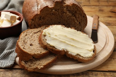 Photo of Fresh bread with butter and knife on wooden table, closeup