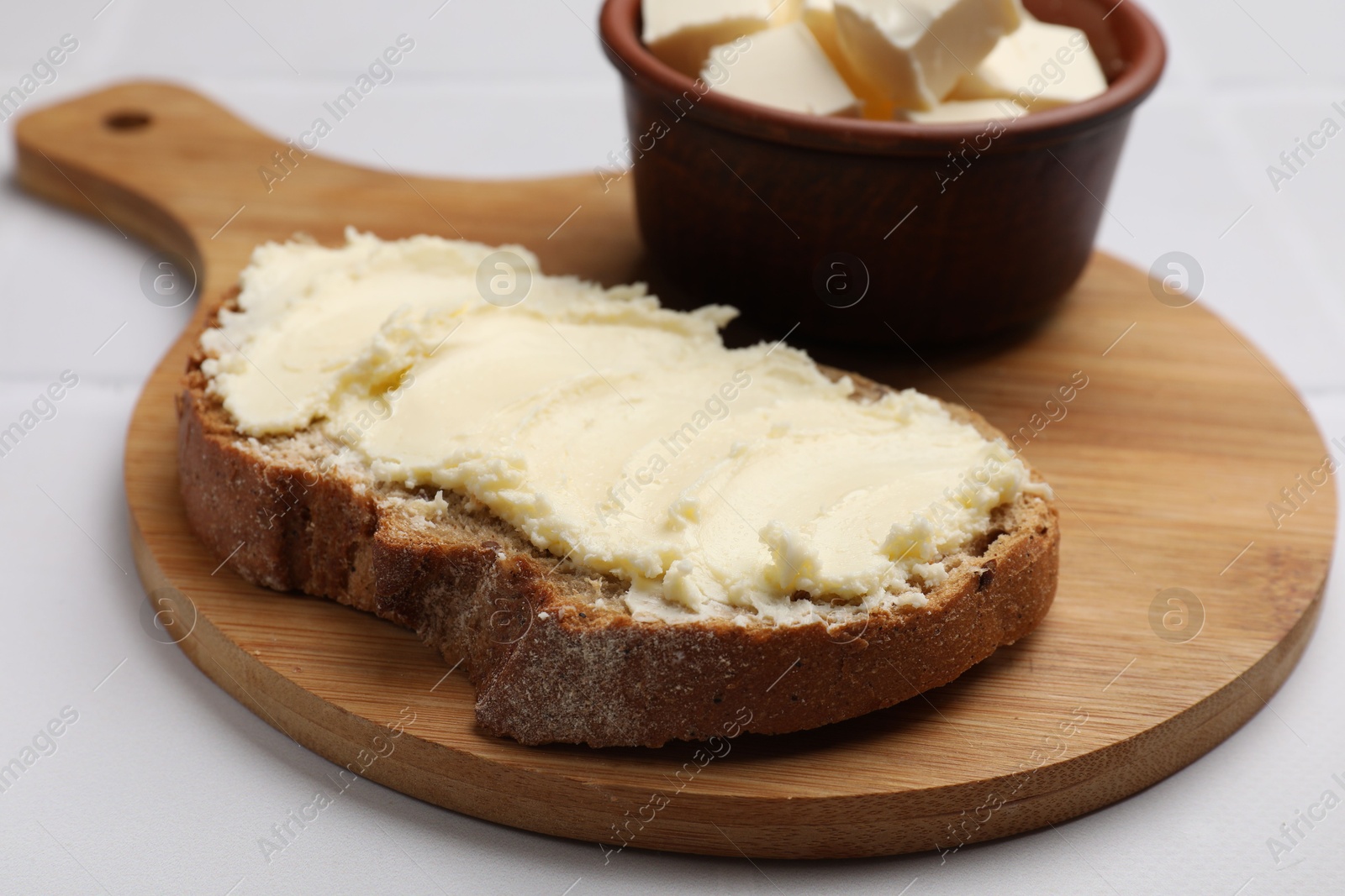 Photo of Fresh bread with butter on white tiled table, closeup