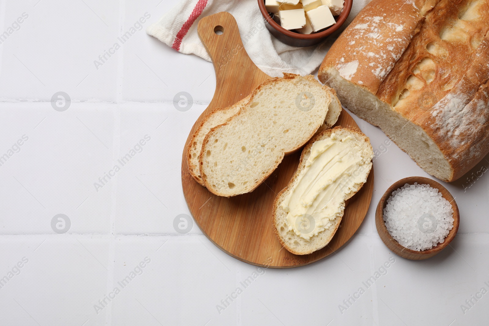 Photo of Fresh bread with butter on white tiled table, flat lay. Space for text