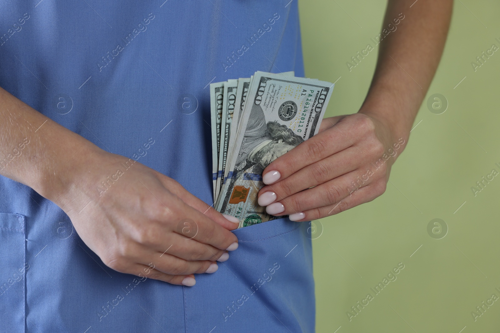 Photo of Corruption concept. Doctor putting dollar banknotes into her pocket on green background, closeup