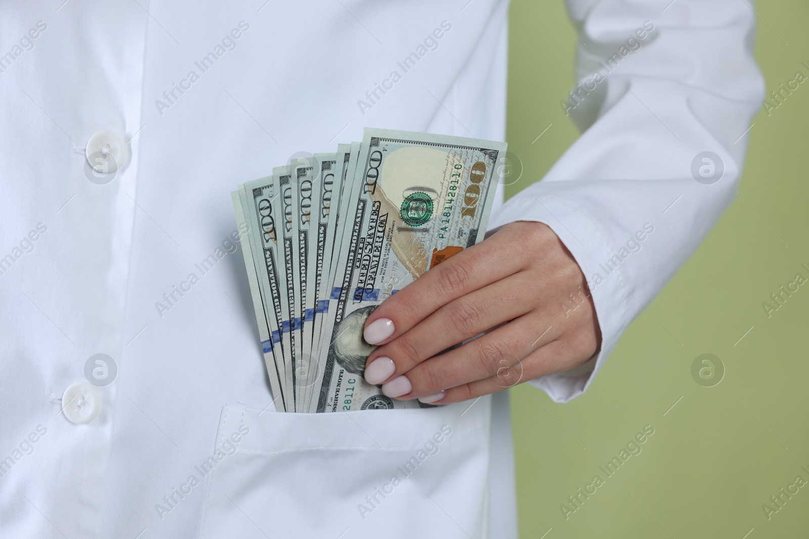 Photo of Corruption concept. Doctor putting dollar banknotes into her pocket on green background, closeup