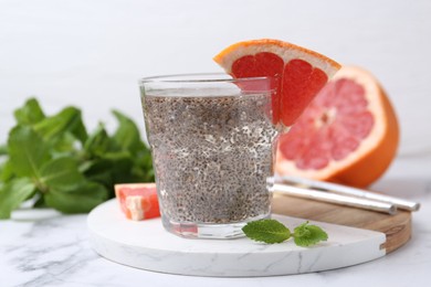 Glass of drink with chia seeds and grapefruit on white marble table, closeup