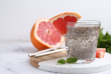 Photo of Glass of drink with chia seeds and grapefruit on white marble table, closeup