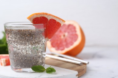 Photo of Glass of drink with chia seeds and grapefruit on white marble table, closeup. Space for text