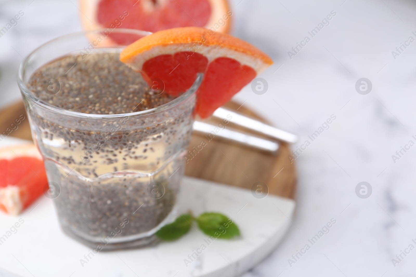 Photo of Glass of drink with chia seeds and grapefruit on white marble table, closeup. Space for text