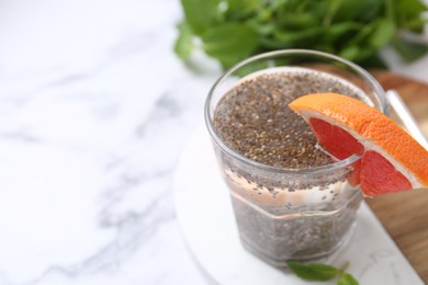 Photo of Glass of drink with chia seeds and grapefruit on white marble table, closeup. Space for text