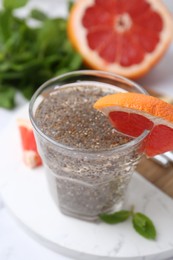 Photo of Glass of drink with chia seeds and grapefruit on white marble table, closeup