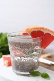 Photo of Glass of drink with chia seeds and grapefruit on white marble table, closeup