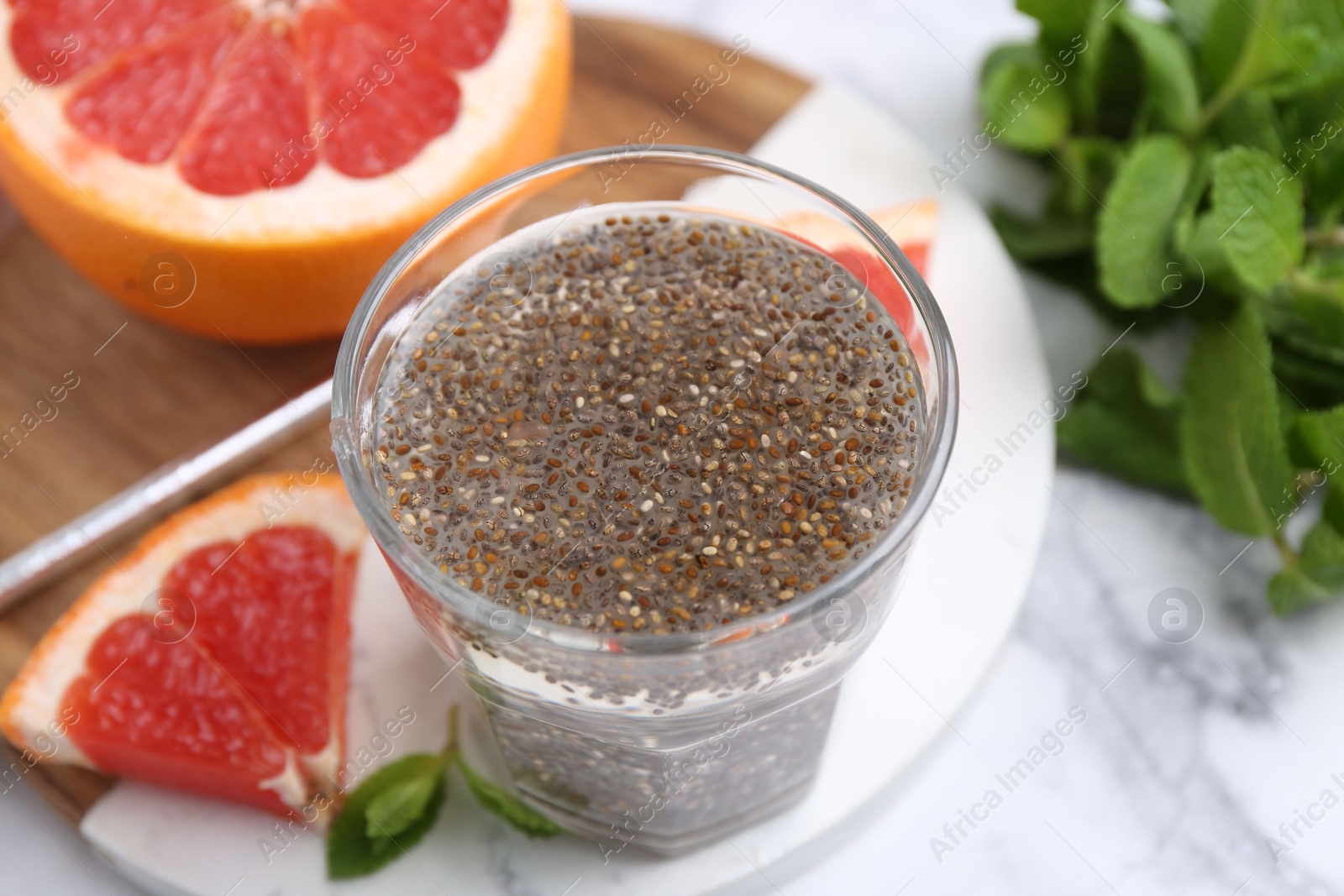 Photo of Glass of drink with chia seeds and grapefruit on white marble table, closeup