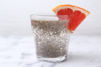 Photo of Glass of drink with chia seeds and grapefruit on white marble table, closeup