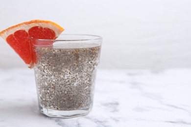 Photo of Glass of drink with chia seeds and grapefruit on white marble table, closeup. Space for text