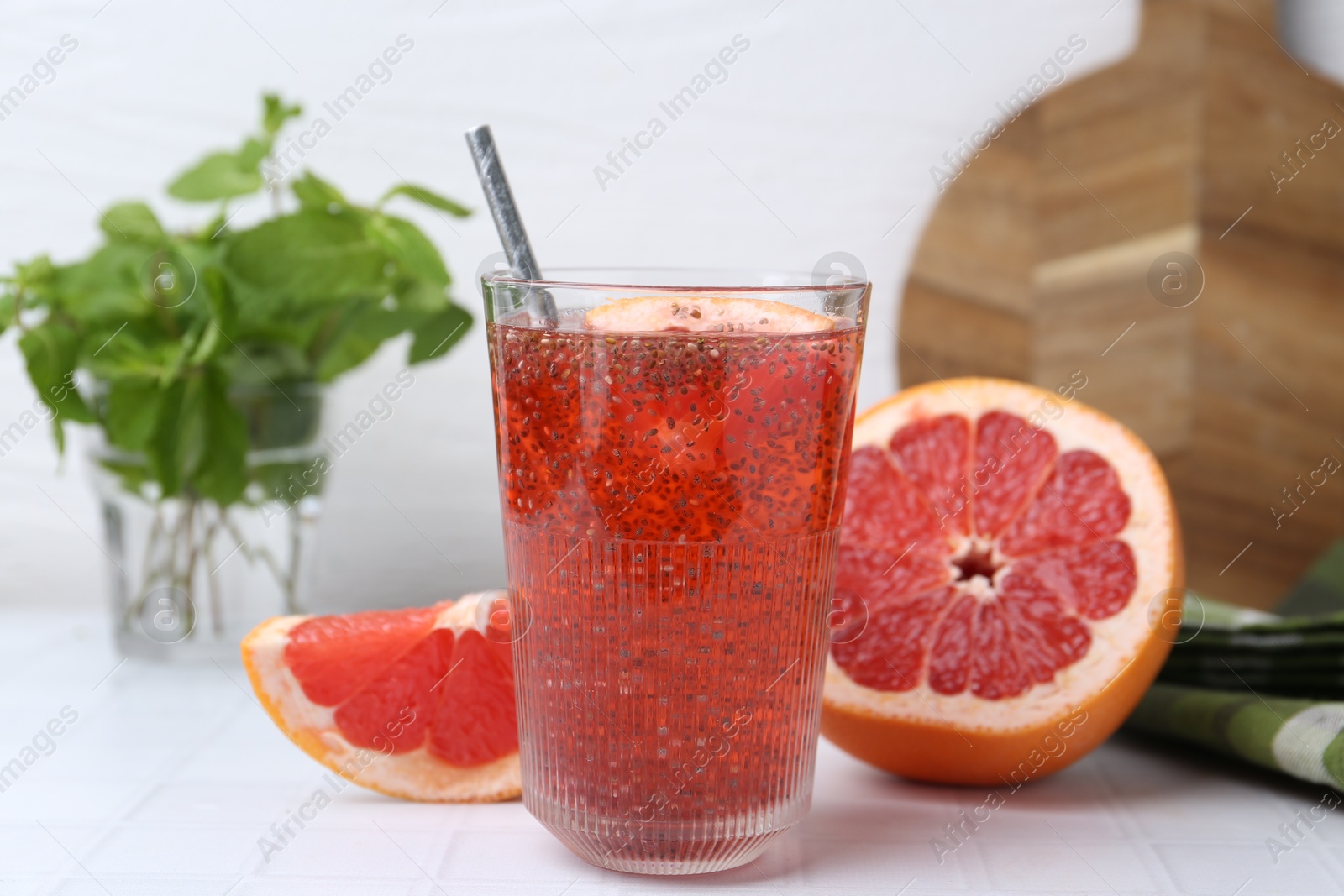 Photo of Glass of drink with chia seeds and grapefruit on white tiled table, closeup