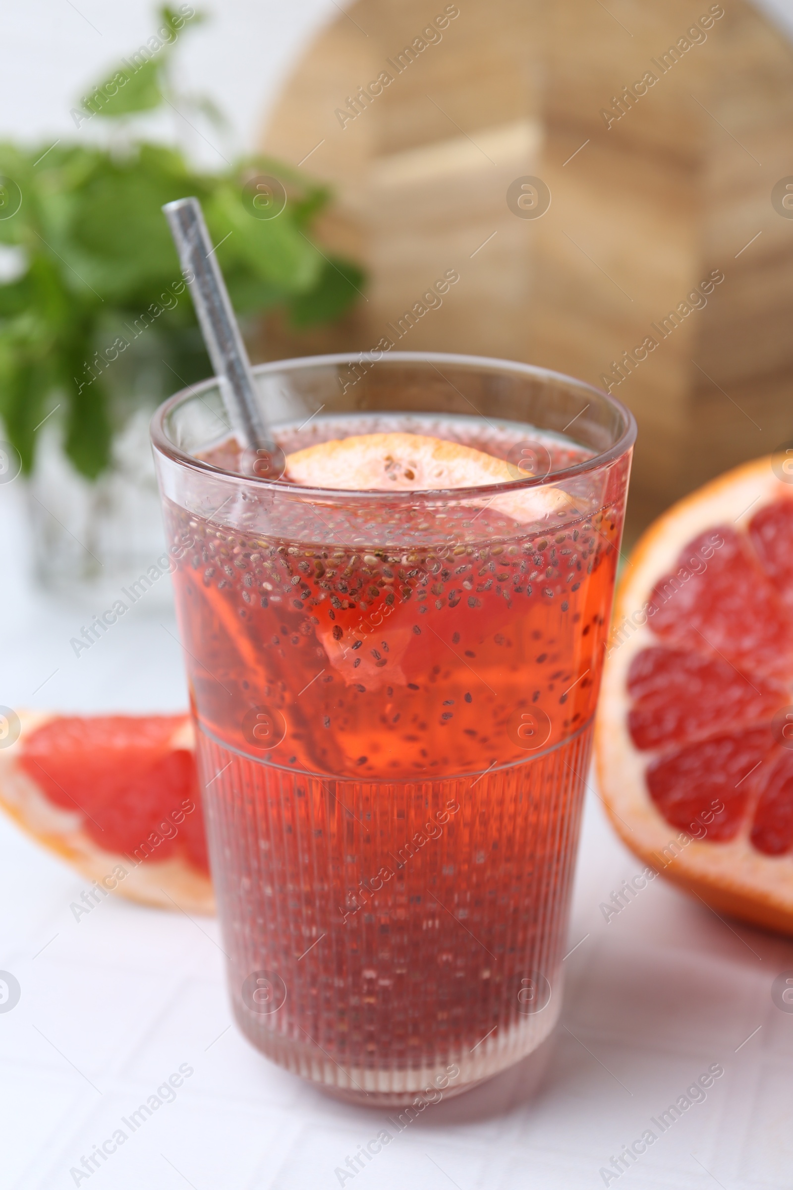 Photo of Glass of drink with chia seeds and grapefruit on white tiled table, closeup