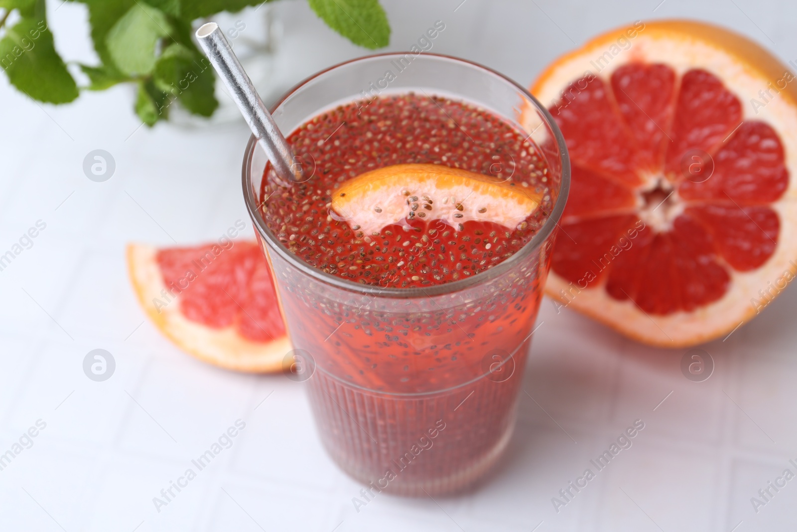 Photo of Glass of drink with chia seeds and grapefruit on white tiled table, closeup