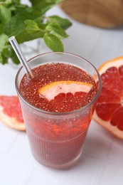 Photo of Glass of drink with chia seeds and grapefruit on white tiled table, closeup