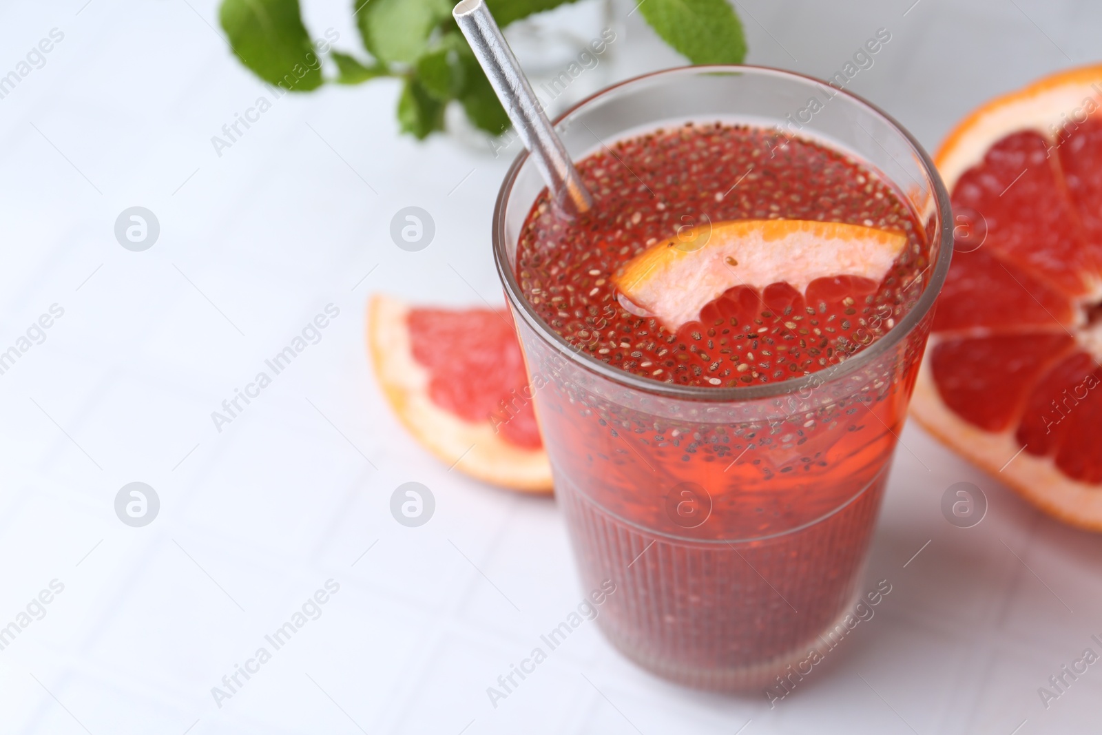 Photo of Glass of drink with chia seeds and grapefruit on white tiled table, closeup. Space for text