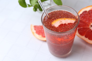 Photo of Glass of drink with chia seeds and grapefruit on white tiled table, closeup. Space for text