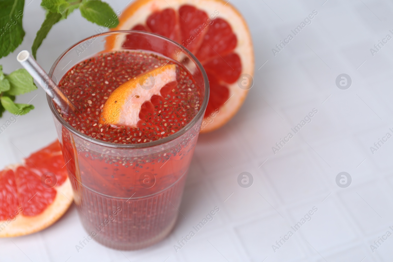 Photo of Glass of drink with chia seeds and grapefruit on white tiled table, closeup. Space for text
