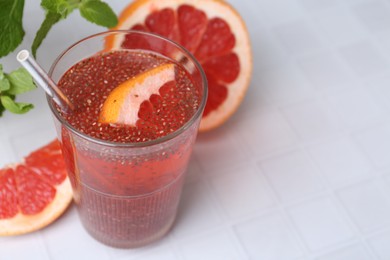 Photo of Glass of drink with chia seeds and grapefruit on white tiled table, closeup. Space for text