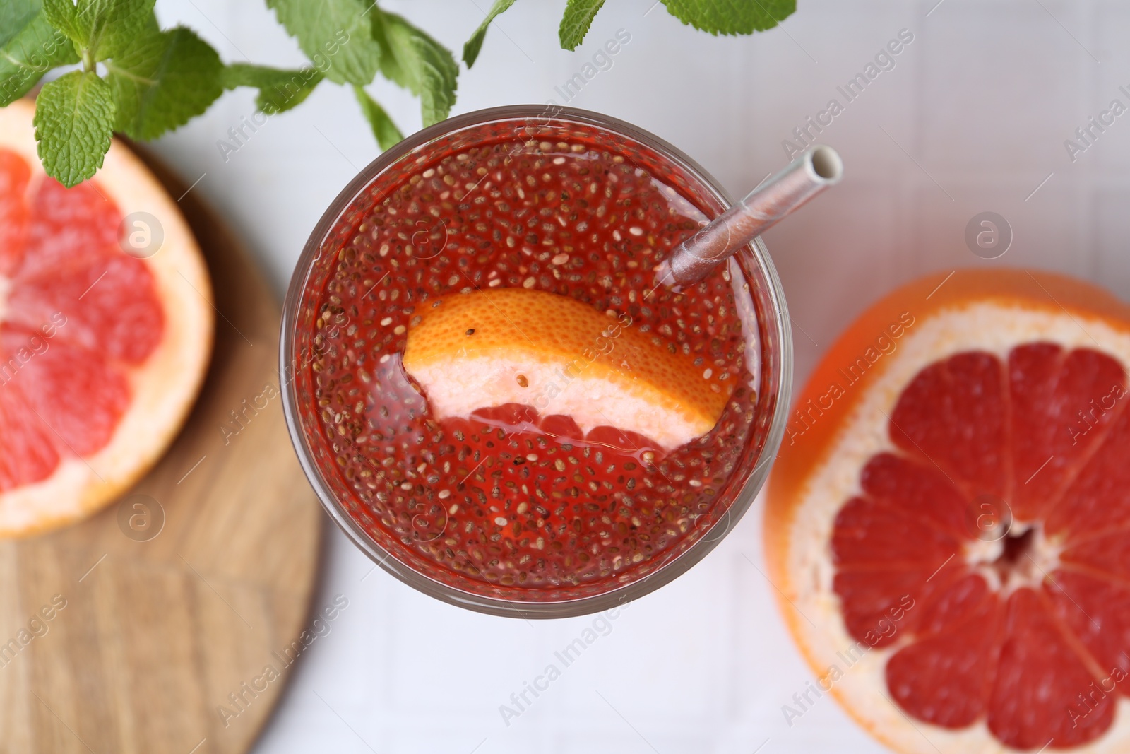 Photo of Glass of drink with chia seeds and grapefruit on white tiled table, flat lay