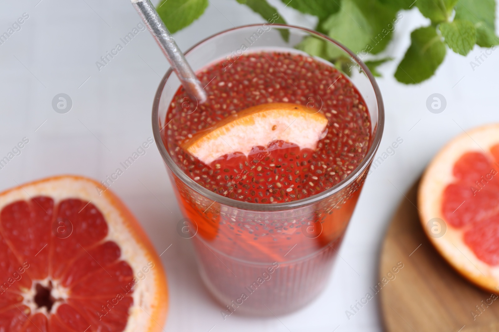 Photo of Glass of drink with chia seeds and grapefruit on white tiled table, closeup