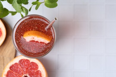 Photo of Glass of drink with chia seeds and grapefruit on white tiled table, flat lay. Space for text