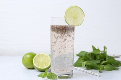 Photo of Glass of drink with chia seeds and lime on white table, closeup