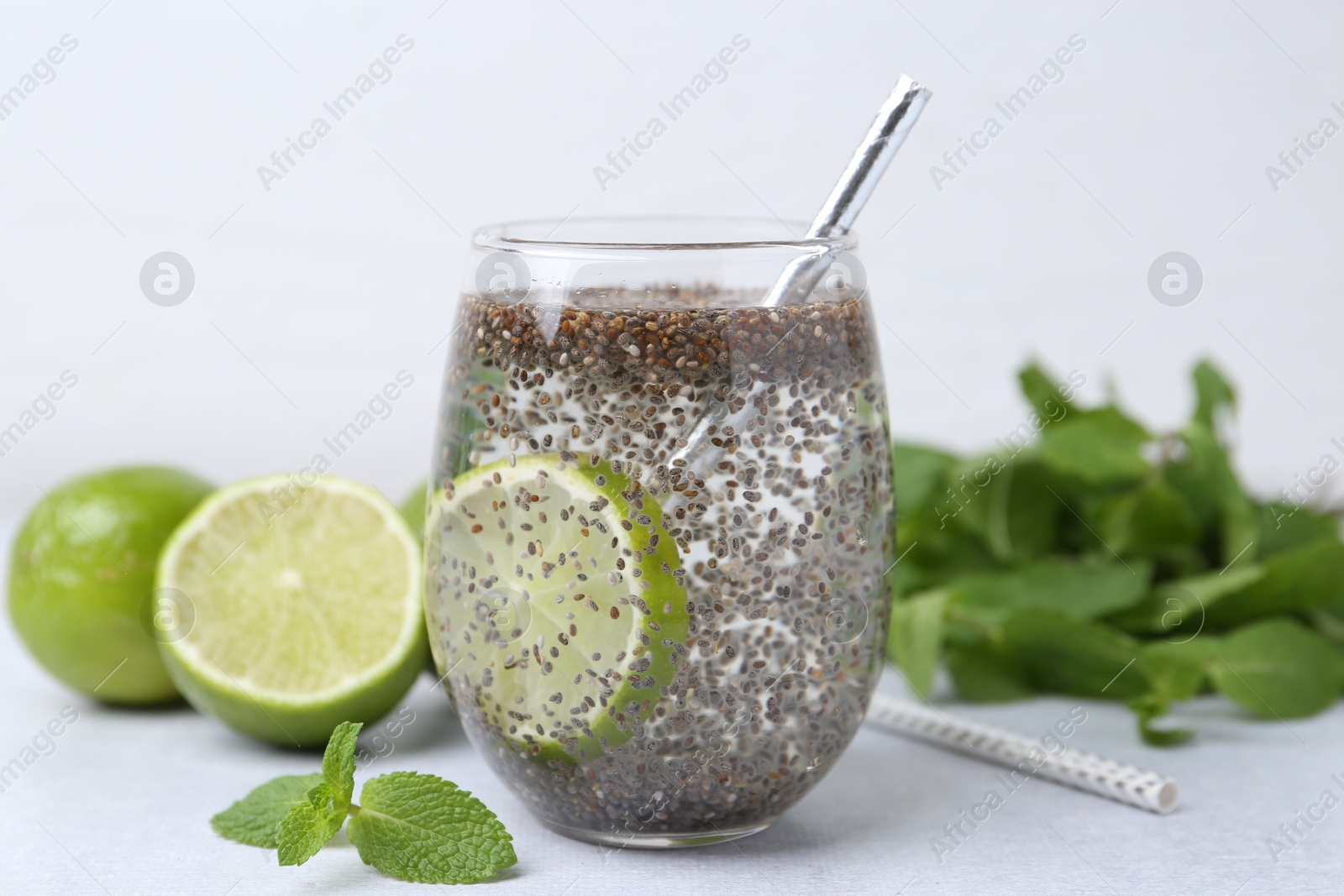 Photo of Glass of drink with chia seeds and lime on white table, closeup