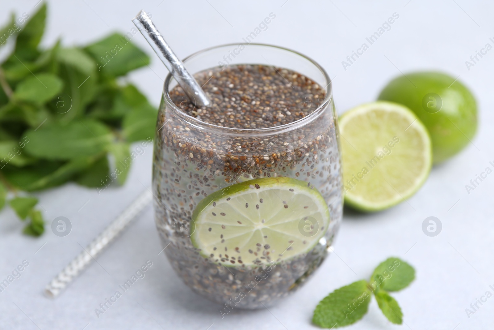 Photo of Glass of drink with chia seeds and lime on white table, closeup