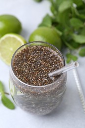 Photo of Glass of drink with chia seeds and lime on white table, closeup