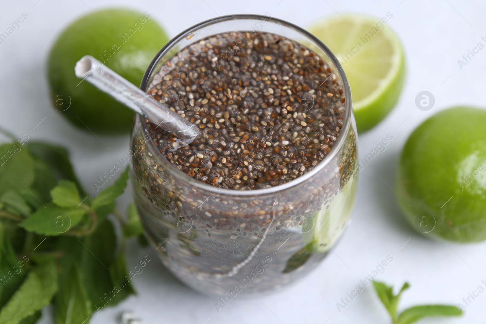 Photo of Glass of drink with chia seeds and lime on white table, closeup