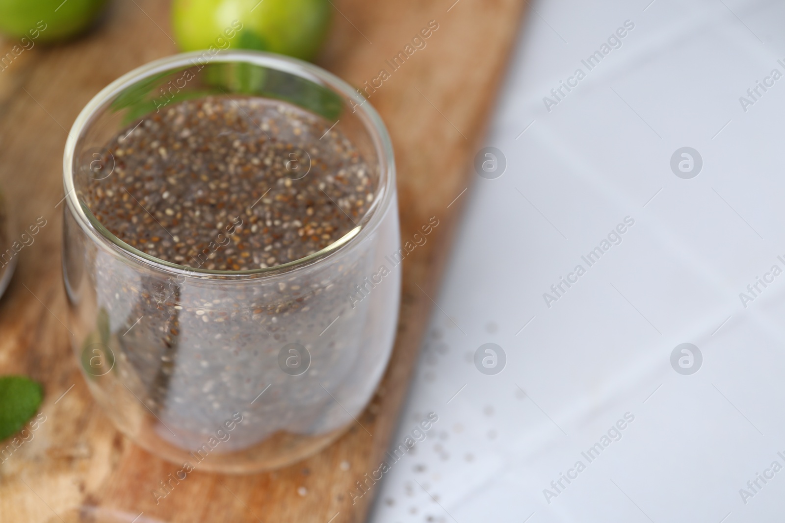 Photo of Glass of drink with chia seeds and lime on white tiled table, closeup. Space for text