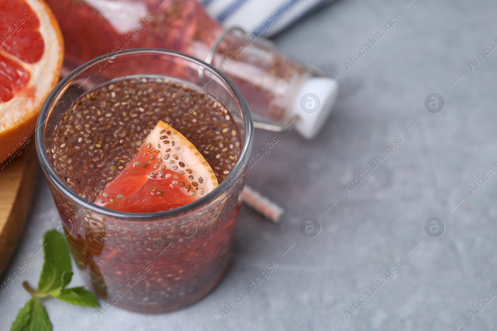 Photo of Glass of drink with chia seeds and grapefruit on grey table, closeup. Space for text