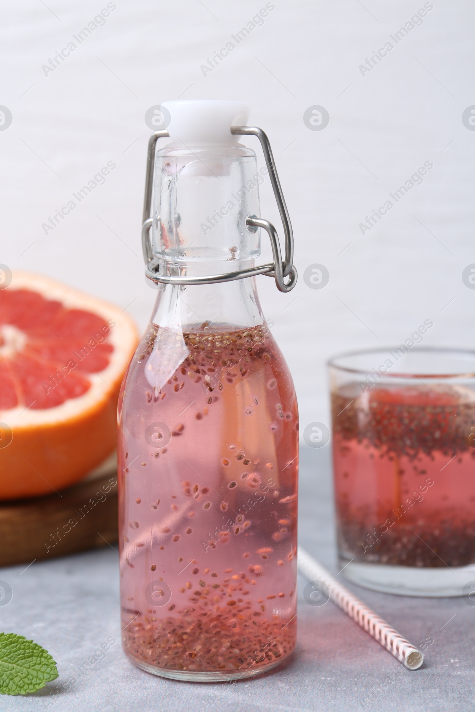 Photo of Glass bottle of drink with chia seeds and grapefruit on grey table