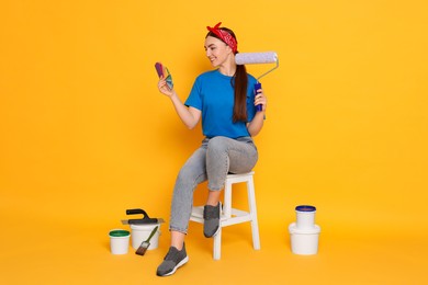 Young decorator with different tools on orange background