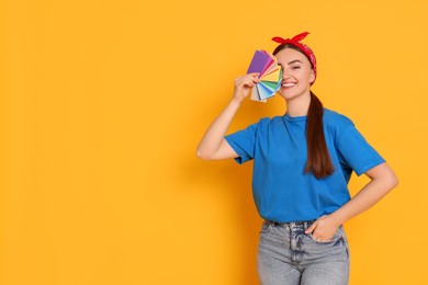 Portrait of young decorator with color palettes on orange background, space for text