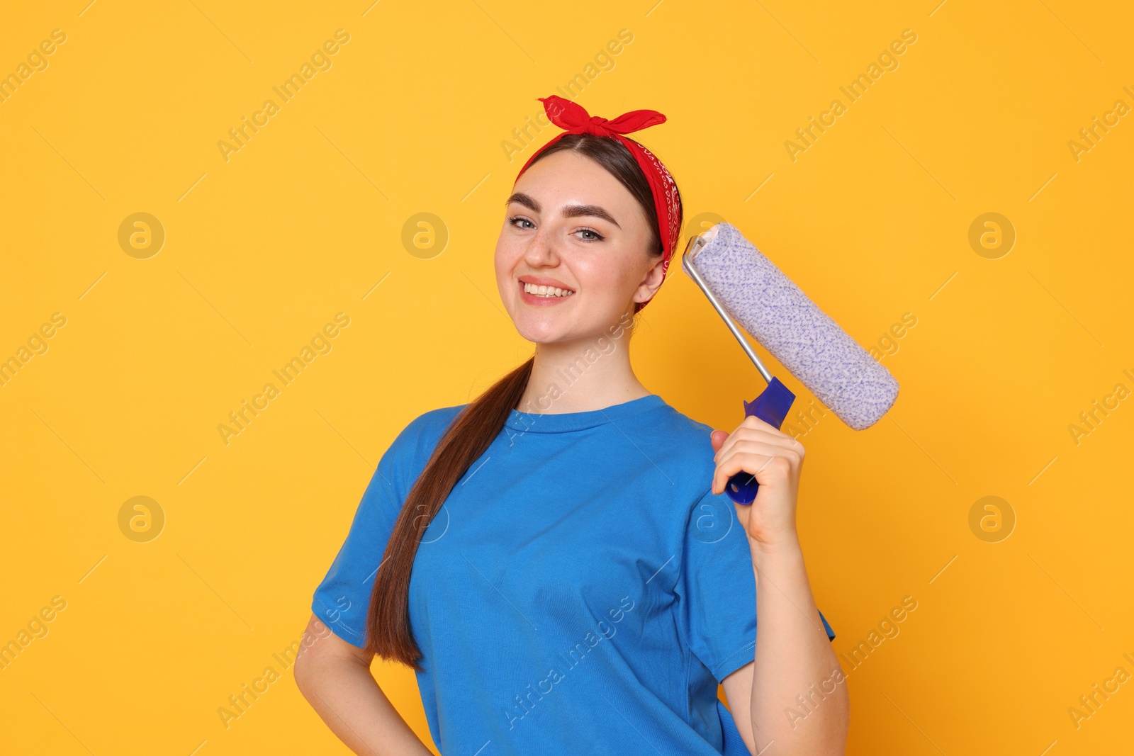 Photo of Portrait of young decorator with paint roller on orange background