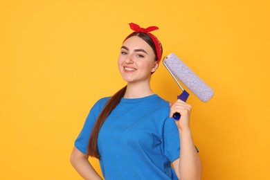 Portrait of young decorator with paint roller on orange background