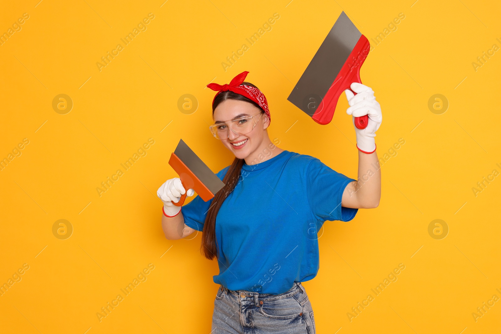 Photo of Portrait of young decorator with putty knives on orange background