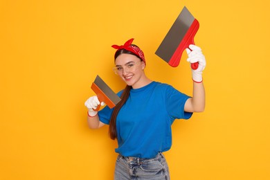 Portrait of young decorator with putty knives on orange background