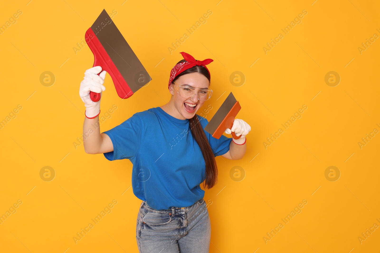 Photo of Portrait of young decorator with putty knives on orange background