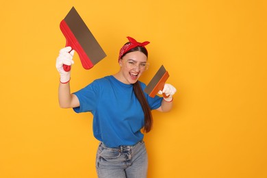 Portrait of young decorator with putty knives on orange background