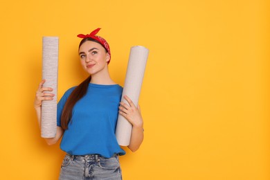 Photo of Young decorator with rolls of wallpaper on orange background, space for text