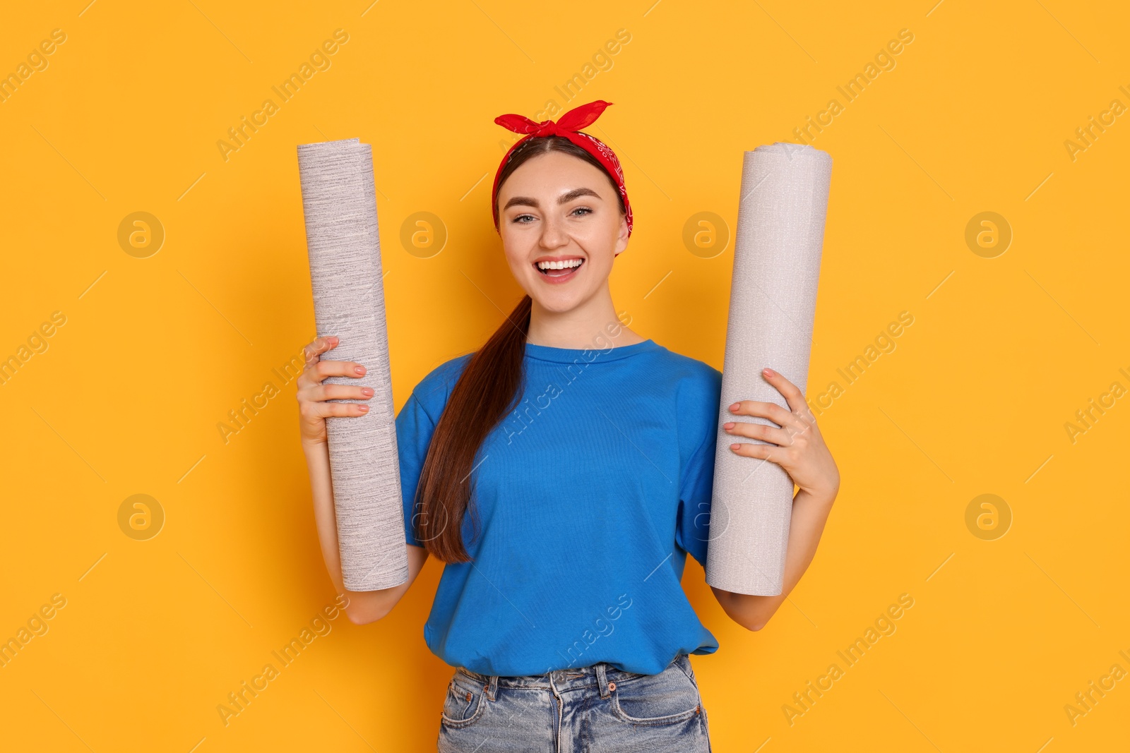 Photo of Young decorator with rolls of wallpaper on orange background