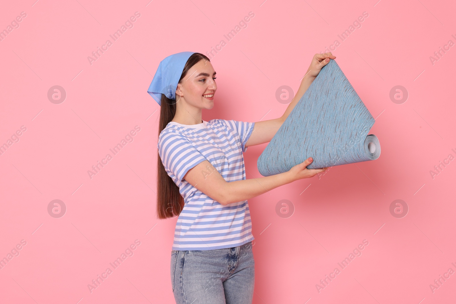 Photo of Young decorator with roll of wallpaper on pink background