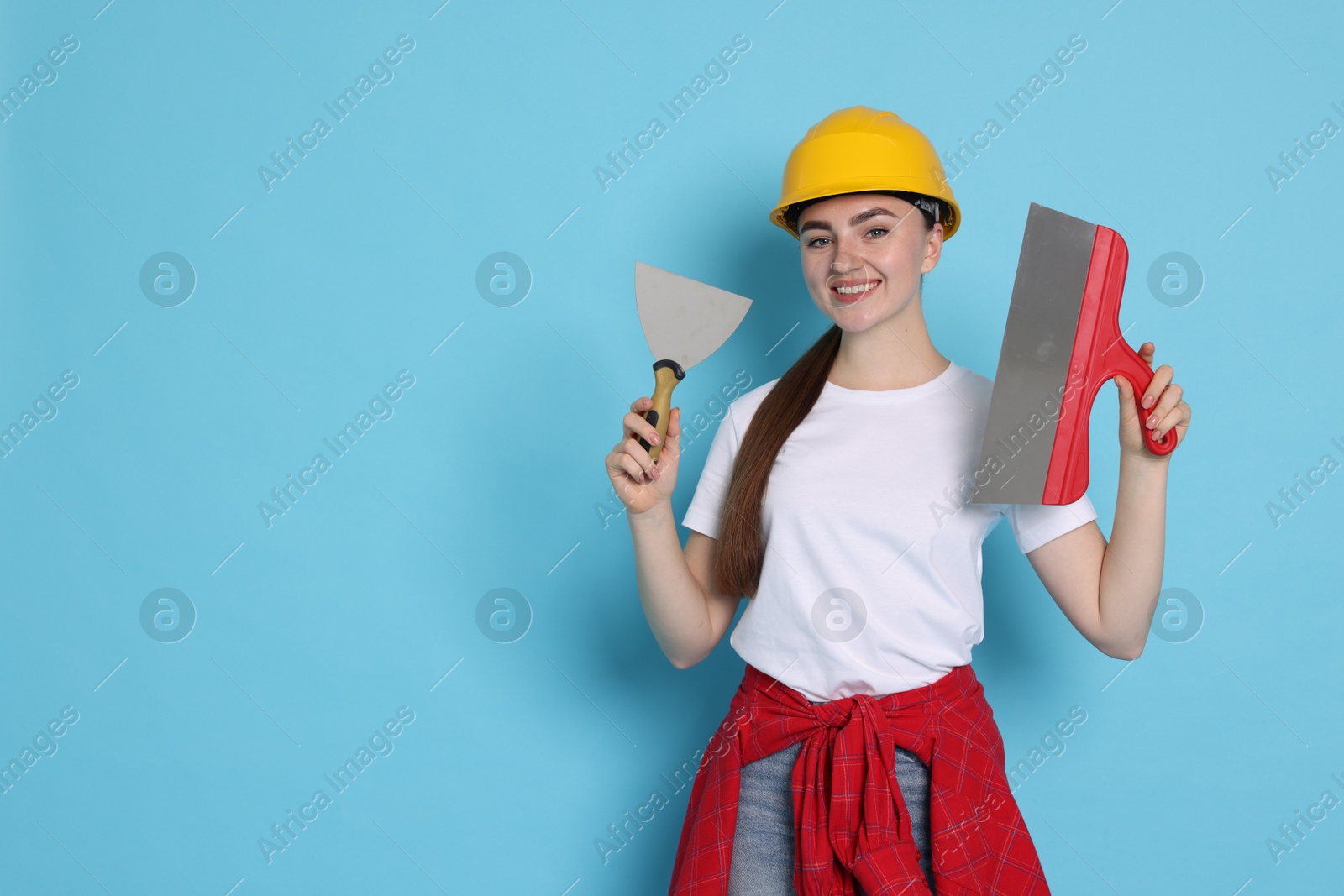 Photo of Portrait of young decorator with putty knives on light blue background, space for text