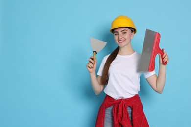 Portrait of young decorator with putty knives on light blue background, space for text